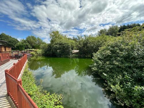 a pond with green water and a red fence at Kingfisher Cosy Lakeside Lodge in Carnforth
