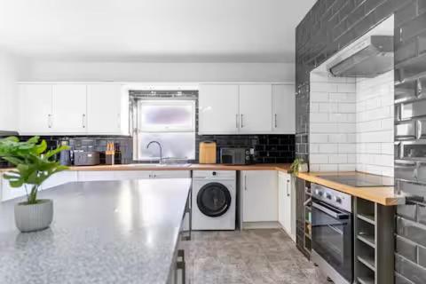 una cocina con gabinetes blancos y una lavadora y secadora en Mauldeth Shared House, en Mánchester