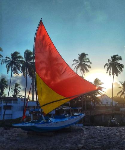 a boat with a red and yellow sail on the beach at Pousada Rio Mar in Maxaranguape