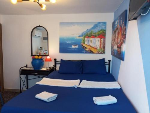 Schlafzimmer mit einem blauen Bett, einem Schreibtisch und einem Gemälde in der Unterkunft 4 Seasons Suites Paradise Athens Airport in Markopoulo