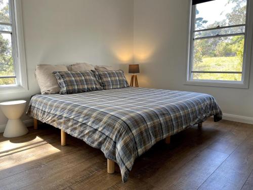 a bedroom with a bed with a plaid blanket and two windows at Happy Mountain House in Blackheath