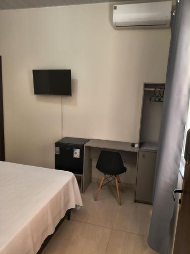 a room with a bed and a desk and a television at suíte para 3 pessoas com ar,tv e frigobar garagem para veículo de pequeno porte in Sinop
