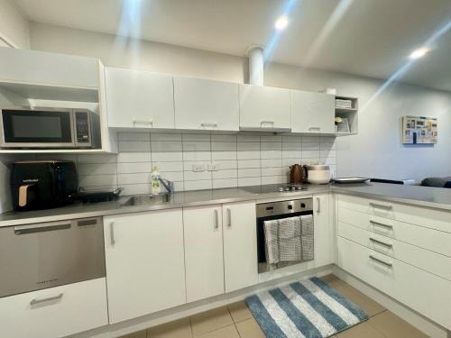 a white kitchen with white cabinets and a microwave at Convenient & Comfortable Apartment Suite in Albany in Auckland