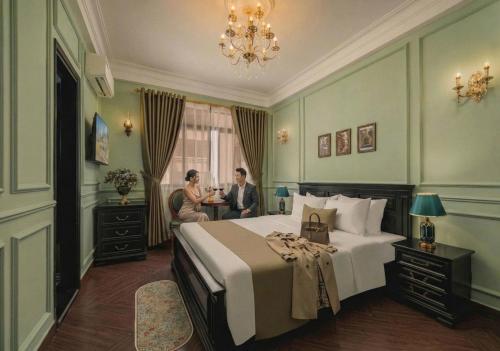 a bedroom with a bed and two people sitting at a table at Vina Vintage Hotel in Hue