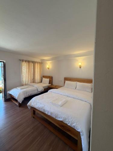 two beds in a hotel room with white sheets at RJ Boutique Hotel - Ghandruk in Astam