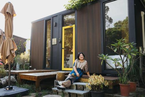 Konggu Valley Retreat Hut X By Tiny Away في T'ou-kou: امرأة تجلس على مقعد أمام منزل صغير