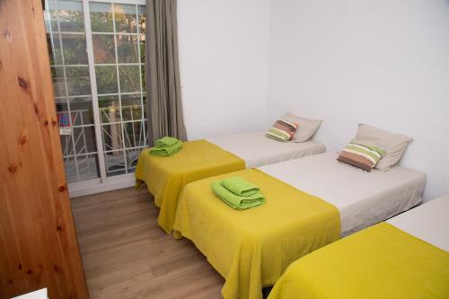 a room with three beds with yellow sheets and a window at GranVia Fira Apartment in Hospitalet de Llobregat