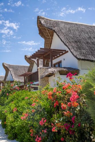 a house with a thatched roof and flowers at Natural Park Villa Resort in Pingwe