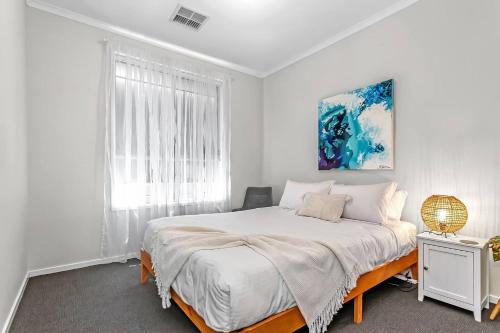 a white bedroom with a bed and a window at Reef Retreat - Modern Beach House Sanctuary in Port Noarlunga