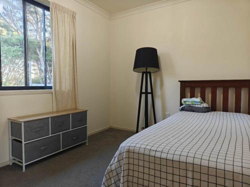 a bedroom with a bed and a lamp and a window at Hearty Acres Farm Cottage in Auckland