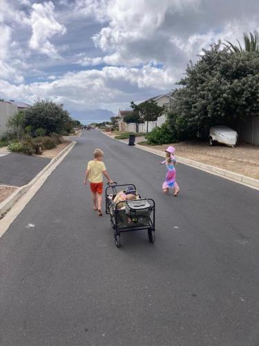 a boy and a girl walking down a street with a cart at Rest@Kommetjie in Cape Town