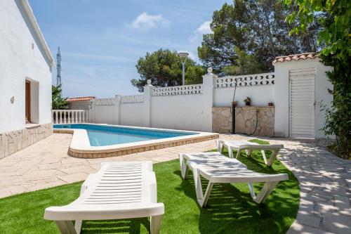 Un patio trasero con piscina y dos bancos blancos. en Hauzify I Vanessa Park, en El Casalot