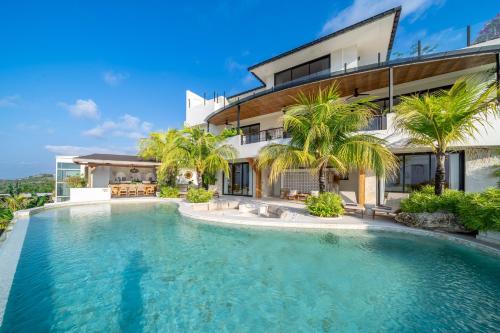 a swimming pool in front of a house with palm trees at Casa Daria Sofia - Ocean Views Infinity Pool Escape with Cinema & Gym in Uluwatu