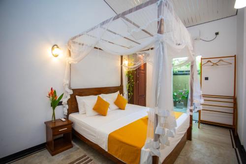 a bedroom with a white canopy bed with yellow pillows at Sleeper Wood Villa in Unawatuna