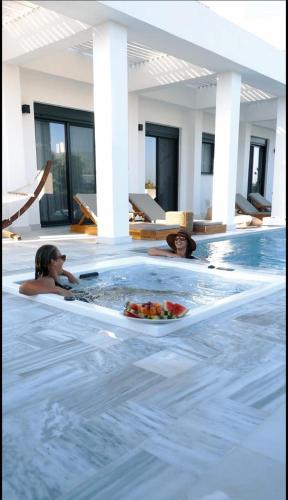 two people in a swimming pool with a plate of food at Seashell Villa - Luxury Pool Retreat - 150m Beach in Lachania