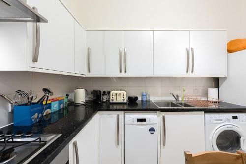 a kitchen with white cabinets and a dishwasher at Garden flat near Ealing Broadway in London