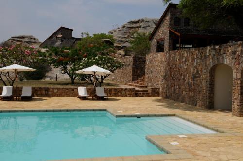 a swimming pool with chairs and umbrellas next to a building at Le Jardin du Roy in Ranohira