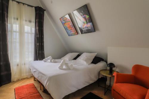 a bedroom with a white bed with a orange chair at Duplex coloré 6 personnes Place des Héros - vue Beffroi - Centre ville in Arras