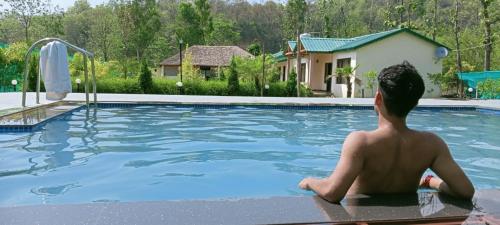 a man sitting in the water in a swimming pool at Corbett Mid Forest House By Havensia Stays in Rāmnagar