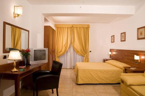 Habitación de hotel con cama, escritorio y TV. en B&B "Bilha Hotel", en Le Castella