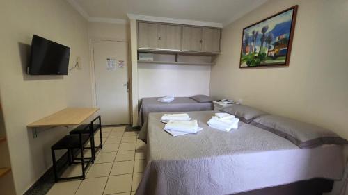 a room with two beds and a table and a television at Flat 8A confortável e completo próximo ao Hot Park e Pousada do Rio Quente in Rio Quente