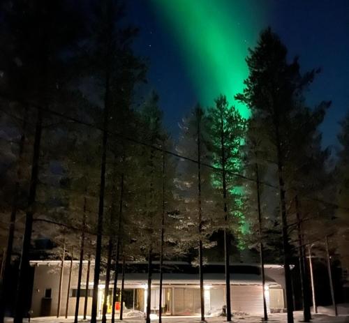 un'aurora sopra un edificio e alberi di notte di Harjunranta a Kuusamo