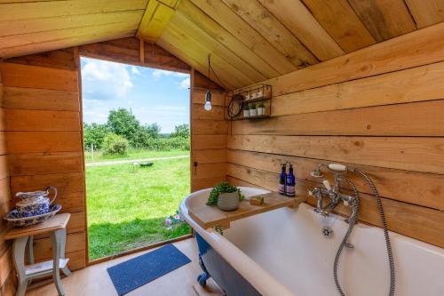 a tub in a wooden bathroom with a window at Leafy Fields Glamping in Ashill