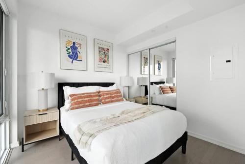 een witte slaapkamer met een groot bed en een spiegel bij Chic Downtown Retreat with Private Patio in Toronto