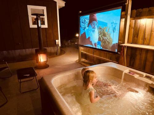 a little girl in a bath tub with a tv at NEW! BEAR Necessities tiny home, outdoor theater! in Garrison
