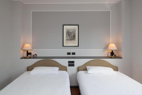 two beds in a room with two lamps on the wall at Hotel Mamiani & Relaxing Spa Urbino in Urbino