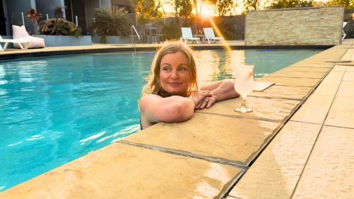 a woman laying on the edge of a swimming pool with a drink at Ramada by Wyndham Hervey Bay in Hervey Bay