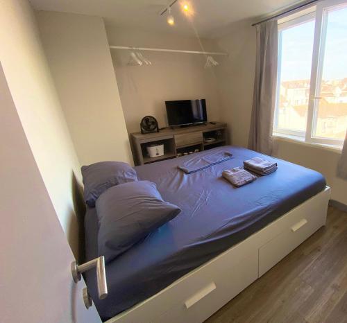 een slaapkamer met een bed met blauwe lakens en een televisie bij Bruges by the Beach in Blankenberge