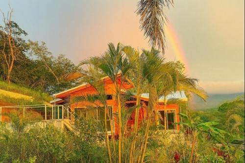 a rainbow in front of a house with palm trees at luxury wooden house mountain view in Hojancha