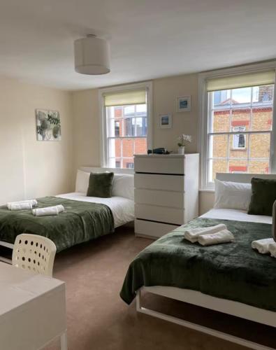 a bedroom with two beds and a dresser and two windows at Lovely Rooms in Camden Town, Central London in London