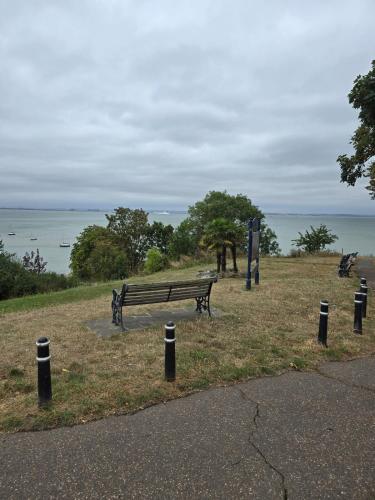 a park bench sitting on the grass near the water at Ivy on Sea Villa in Southend-on-Sea