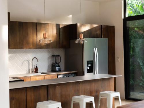 a kitchen with a stainless steel refrigerator and white stools at Nalu Nosara Pool Villa Sombra in Nosara