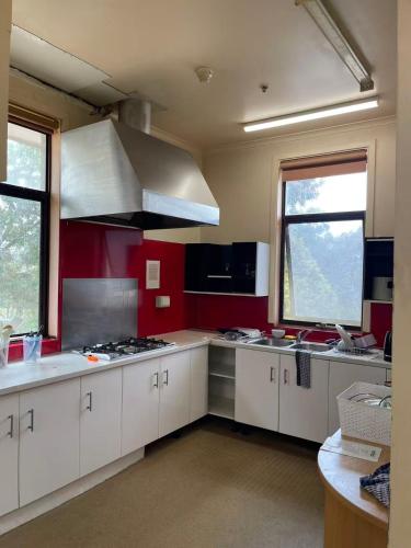 a kitchen with white cabinets and red walls and windows at sj hostel in Legana