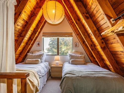 two beds in a room with wooden ceilings at Peaks and Pines Chalet - Ohakune Holiday Home in Ohakune
