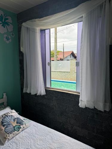 a bedroom with a bed and a window with a view of a pool at Suíte Maresia - Pousada Castelo do Luar in Penha