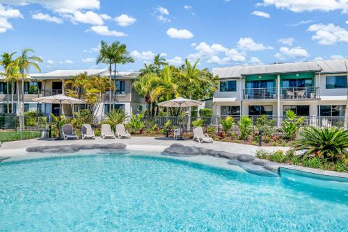 a pool with chairs and umbrellas in front of a building at Ivory Palms Resort Noosa in Noosaville