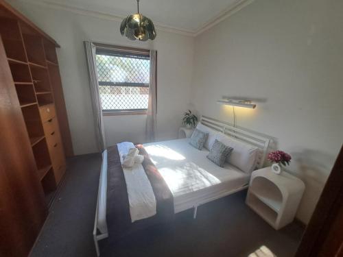 een witte slaapkamer met een bed en een raam bij Relaxing Vintage Cottage in Corrimal