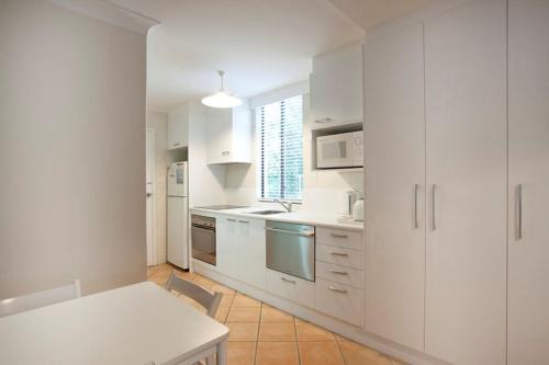 Blueys Beach Villa Manyana 24 في بلويز بيتش: مطبخ أبيض مع دواليب بيضاء وطاولة