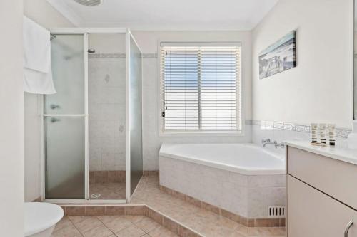 een witte badkamer met een bad en een douche bij Sandy Serenity - Pet Friendly Beach House in The Entrance