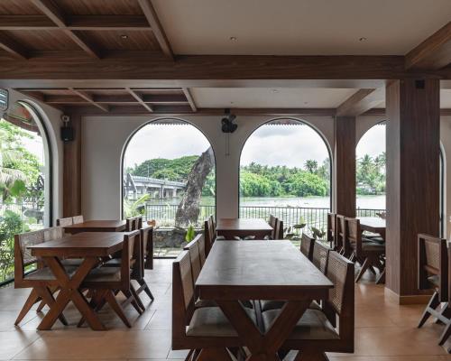 a dining room with tables and chairs and windows at Mayanadhi Resort in Irimbranallūr