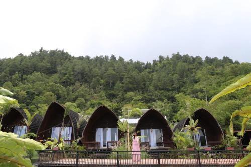 Bukit Delapan Glamping & Coffee في كوبوبانلوكان: صف من الاكواخ مع جبل في الخلف
