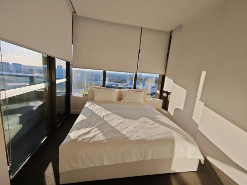 a bedroom with a white bed with large windows at SkyView Stay - Sydney Olympic Park in Sydney