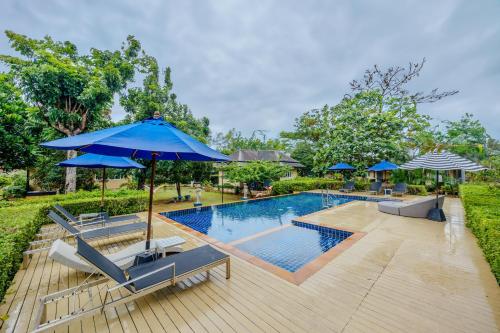 a swimming pool with chairs and a blue umbrella at Perennial Resort in Nai Yang Beach