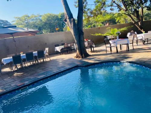 een zwembad met stoelen en tafels en een boom bij Palm Leaf – Hazeldene Kwekwe with pool - 2333 in Kwekwe