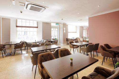 ロンドンにあるQueens Park Premier London Hyde Parkのテーブルと椅子と窓のあるレストラン