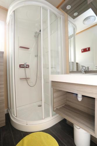 a shower in a bathroom with a sink and a mirror at Camping Le Val de Trie in Béhen